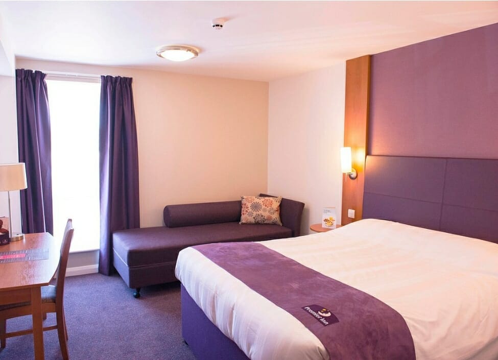 purple bedroom Premier Inn Reading Central Hotel with a bed, table, chair, sofa, and curtains